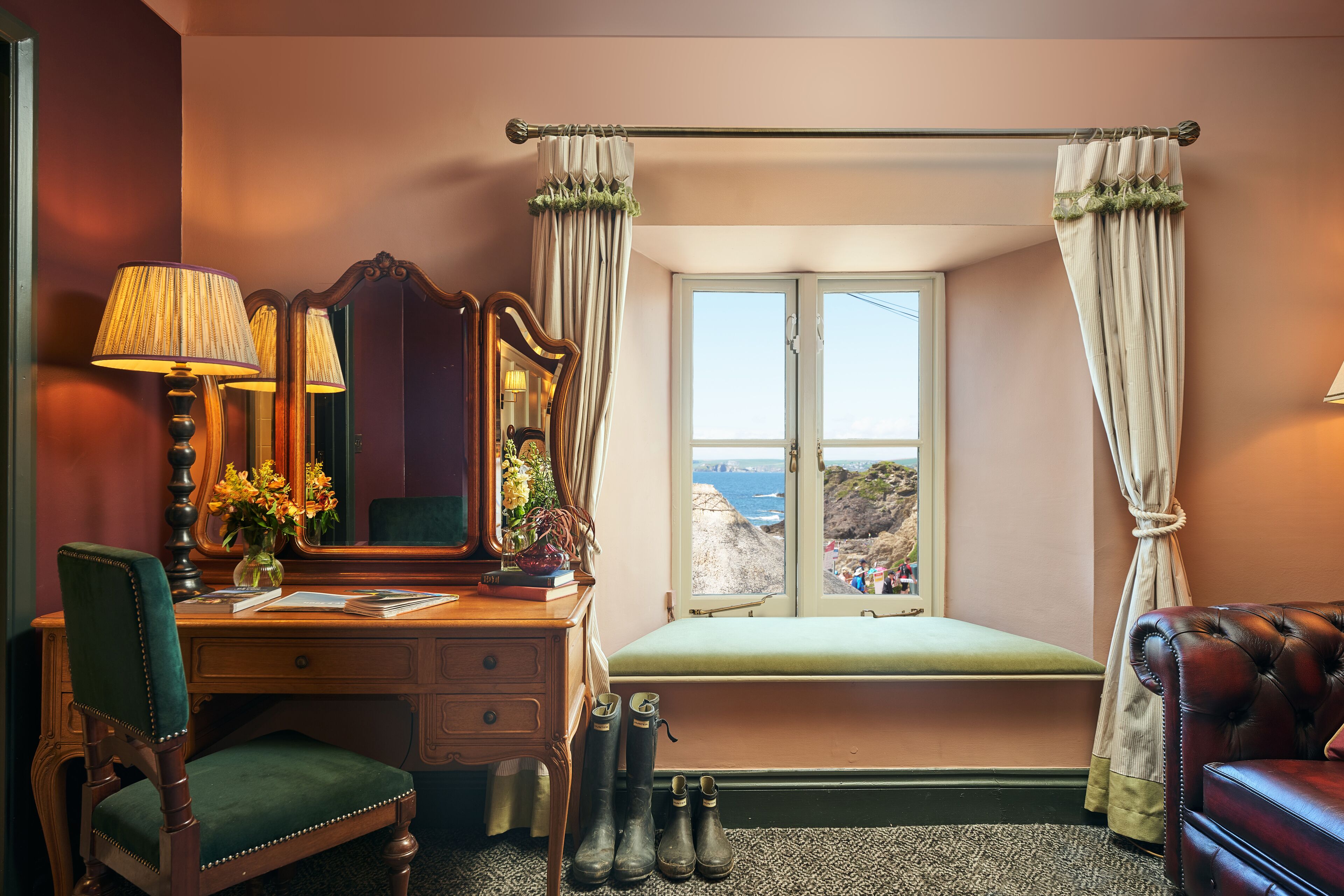 A room with a desk, chair, vanity, and a window with curtains.