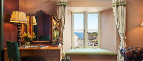 A room with a desk, chair, vanity, and a window with curtains.