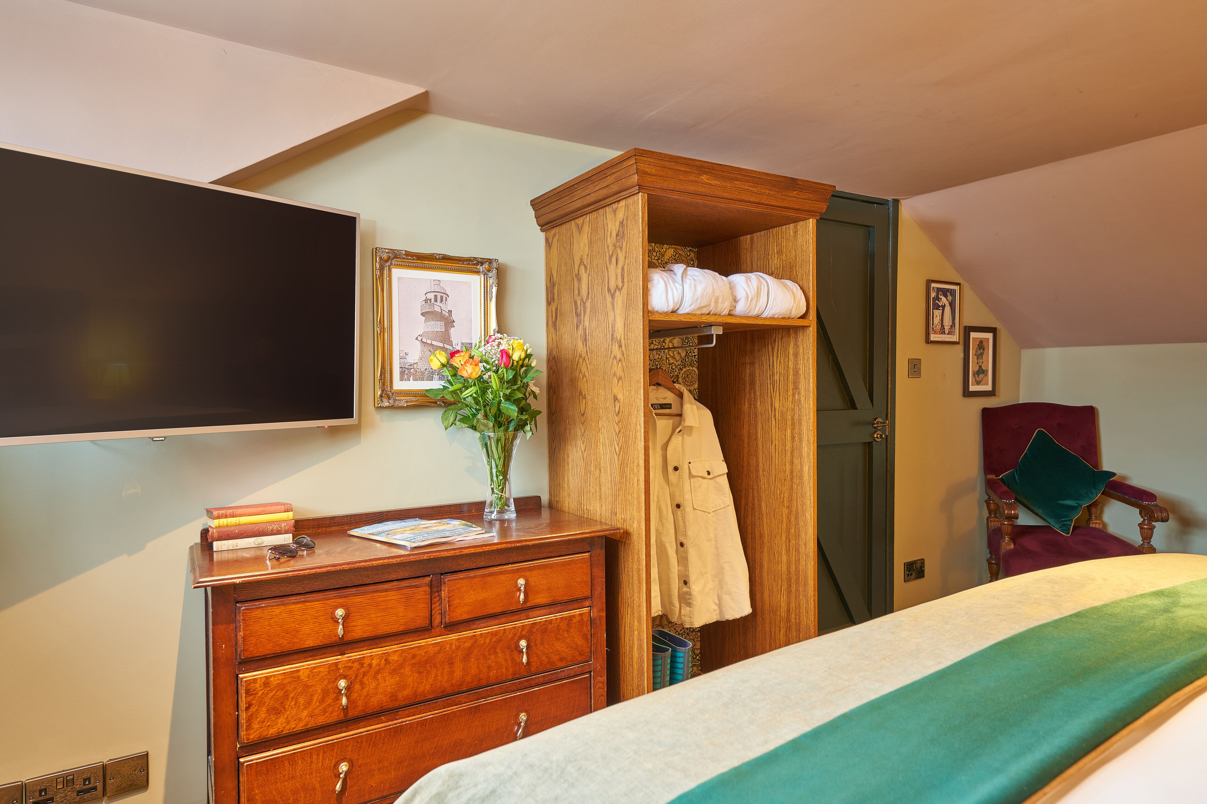 Een slaapkamer met een bed, een houten dressoir, een kapstok, een stoel en een flatscreen televisie.
