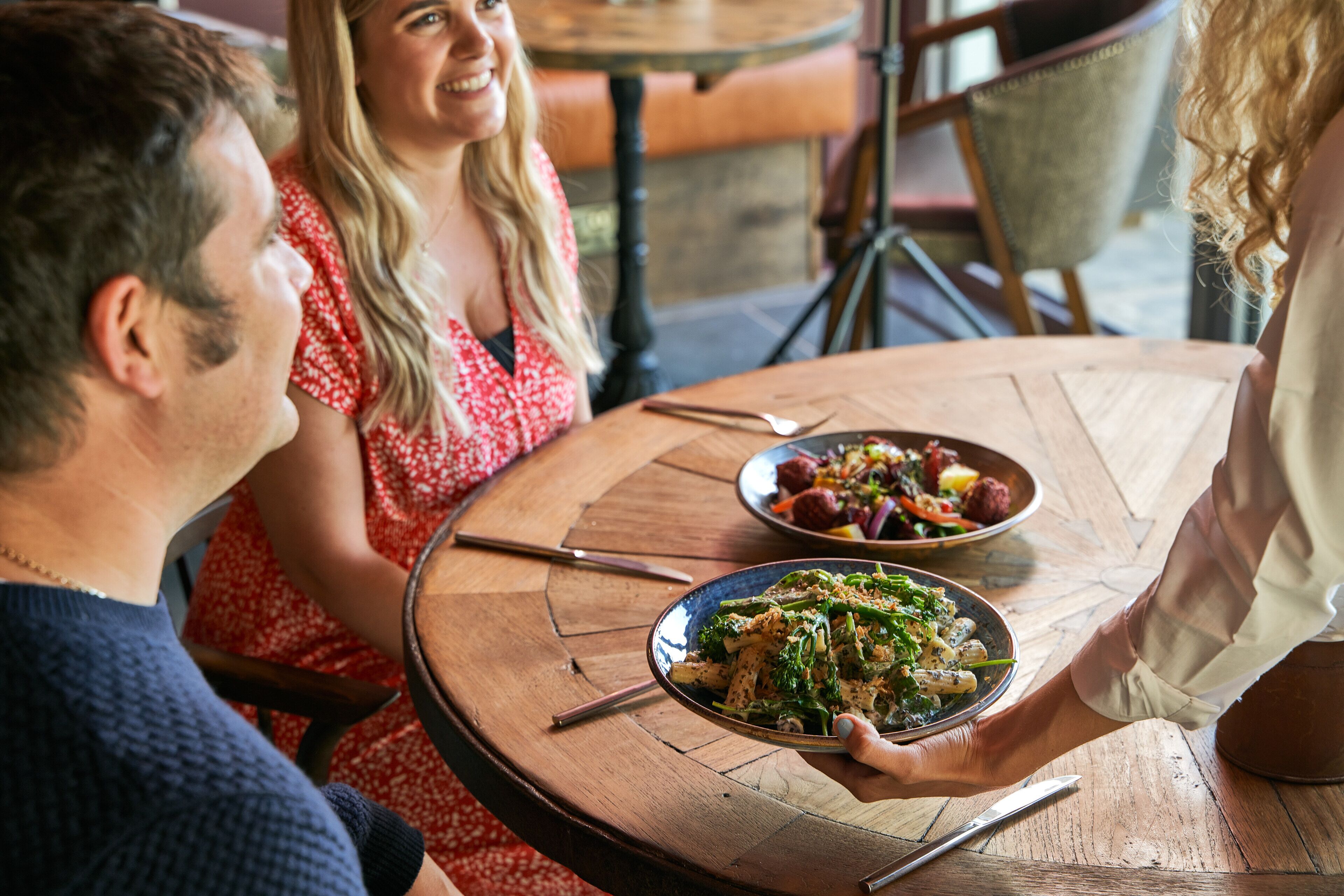 A round wooden table with a plate of food, a knife, and a spoon.