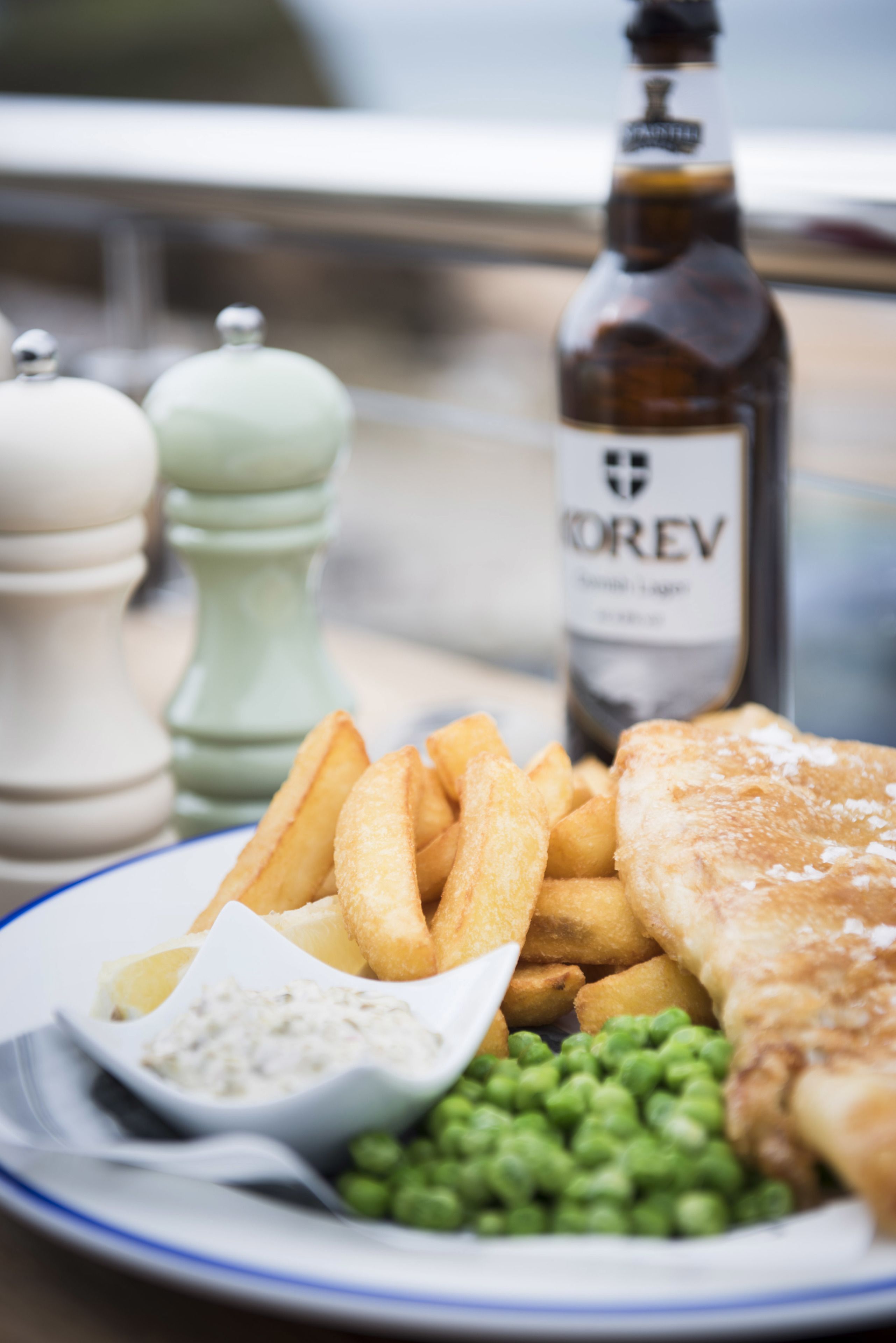 A plate of food including fish, chips, peas, and a dipping sauce, with a bottle of beer in the background.