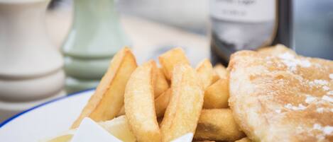 A plate of food including fish, chips, peas, and a dipping sauce, with a bottle of beer in the background.