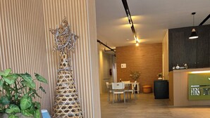 A modern reception area with a wooden reception desk, a white table with a potted plant, and a decorative wall piece. - First Pacific Inn (Davao)