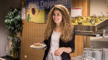 Iemand houdt een bord met eten vast in een kamer met een bordje dat 'Petit Dejeuner' zegt.