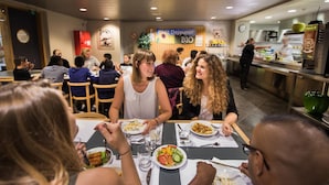 A restaurant with multiple tables, people dining, and a kitchen area in the background.