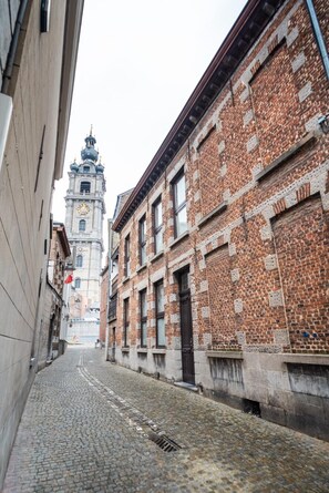 Een straat met keien, langs twee kanten omgeven door historische gebouwen met een klokkentoren in de verte.