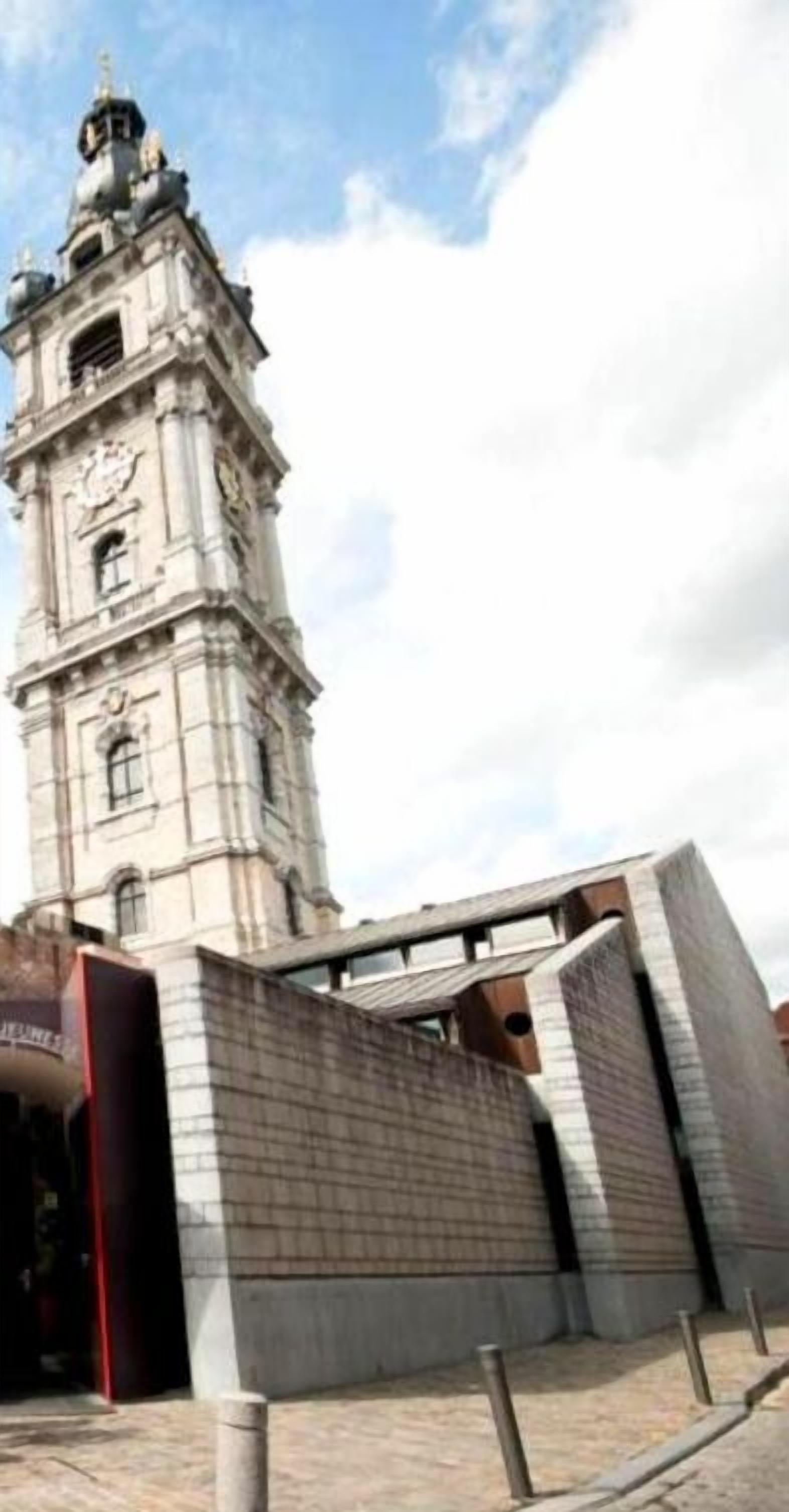 Uma torre histórica com um relógio, rodeada por arquitetura moderna.