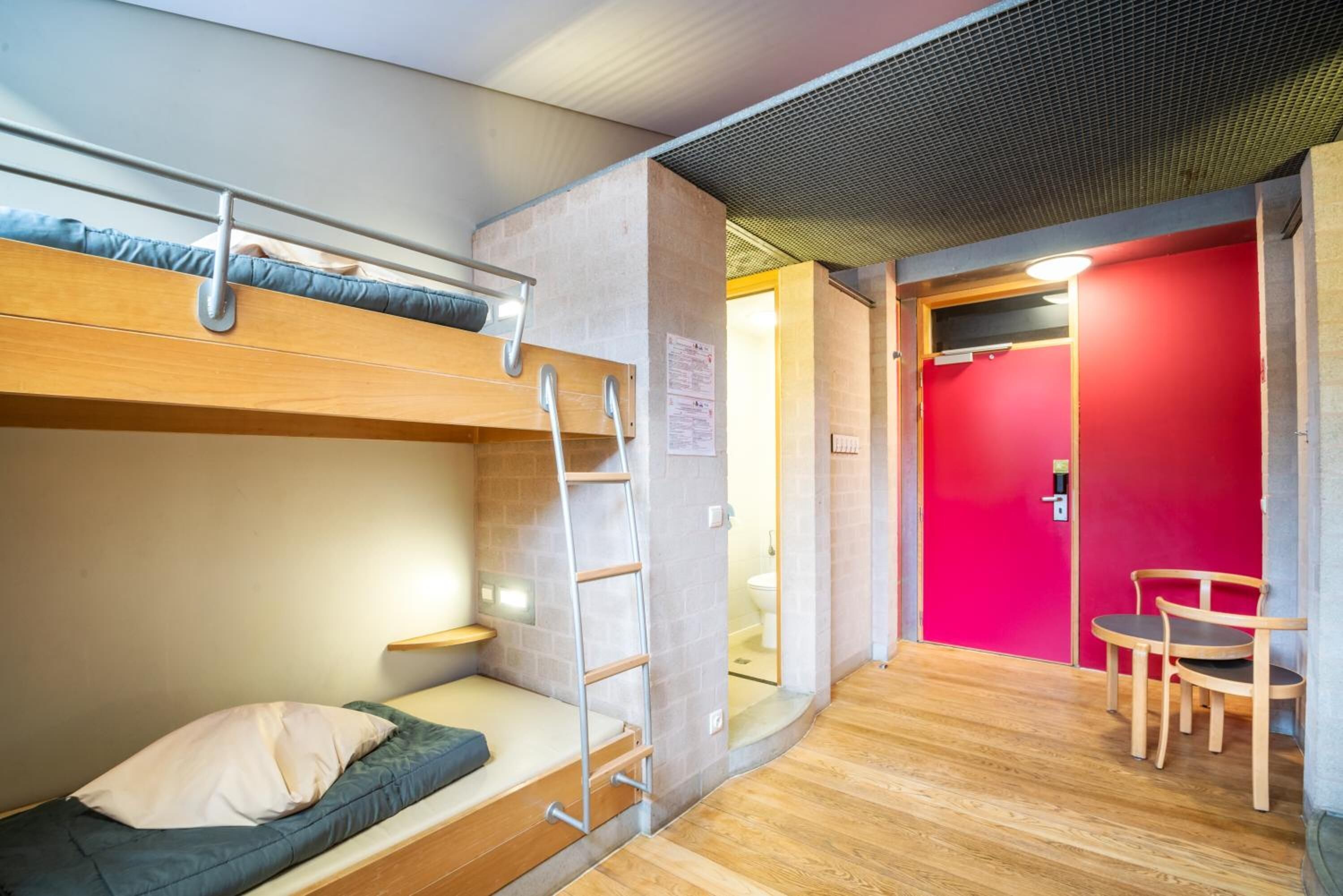 A compact room with bunk beds, a small table, and a red wall.