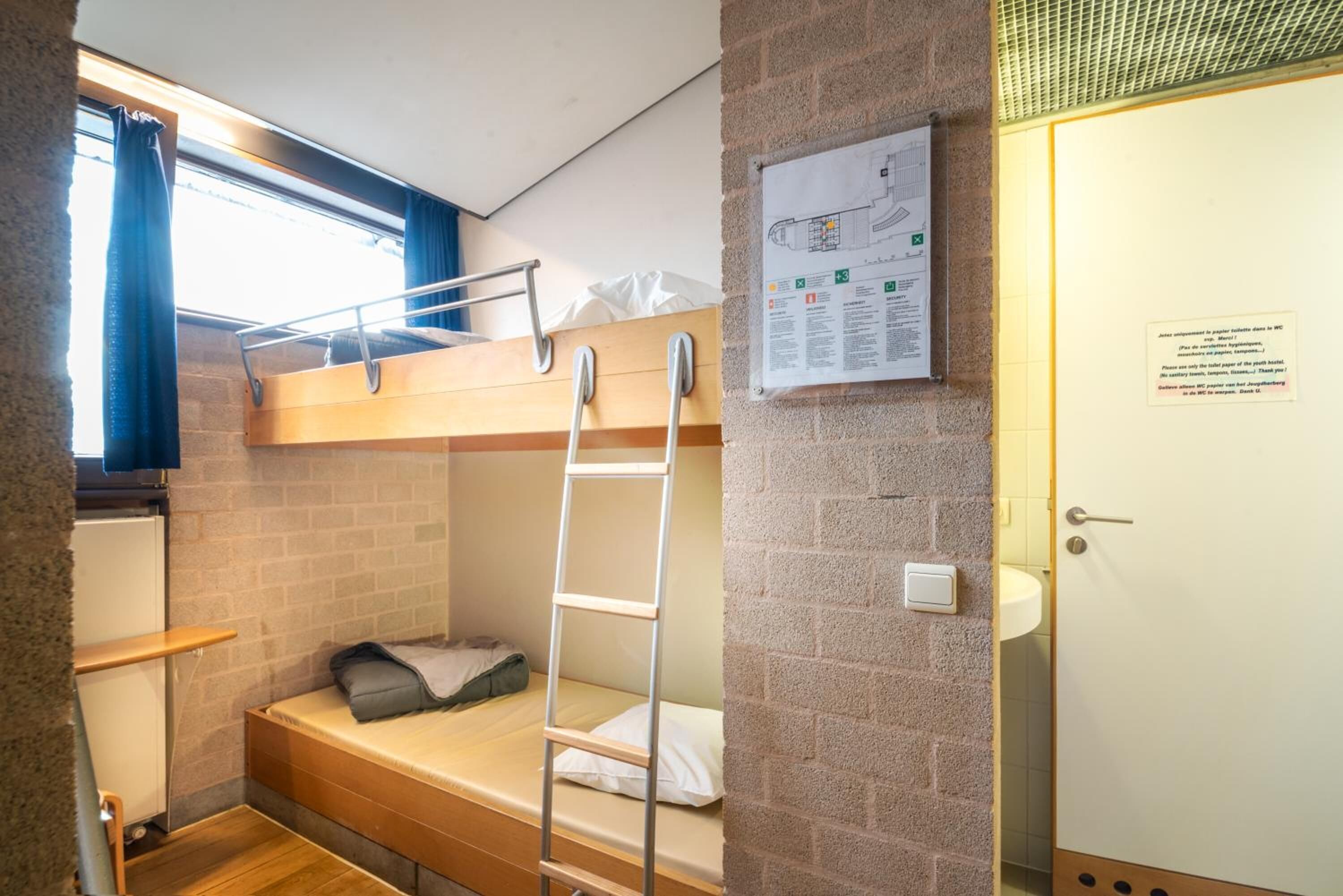 Habitación con literas, una escalera, una ventana con cortinas, un mapa en la pared y una puerta al baño.