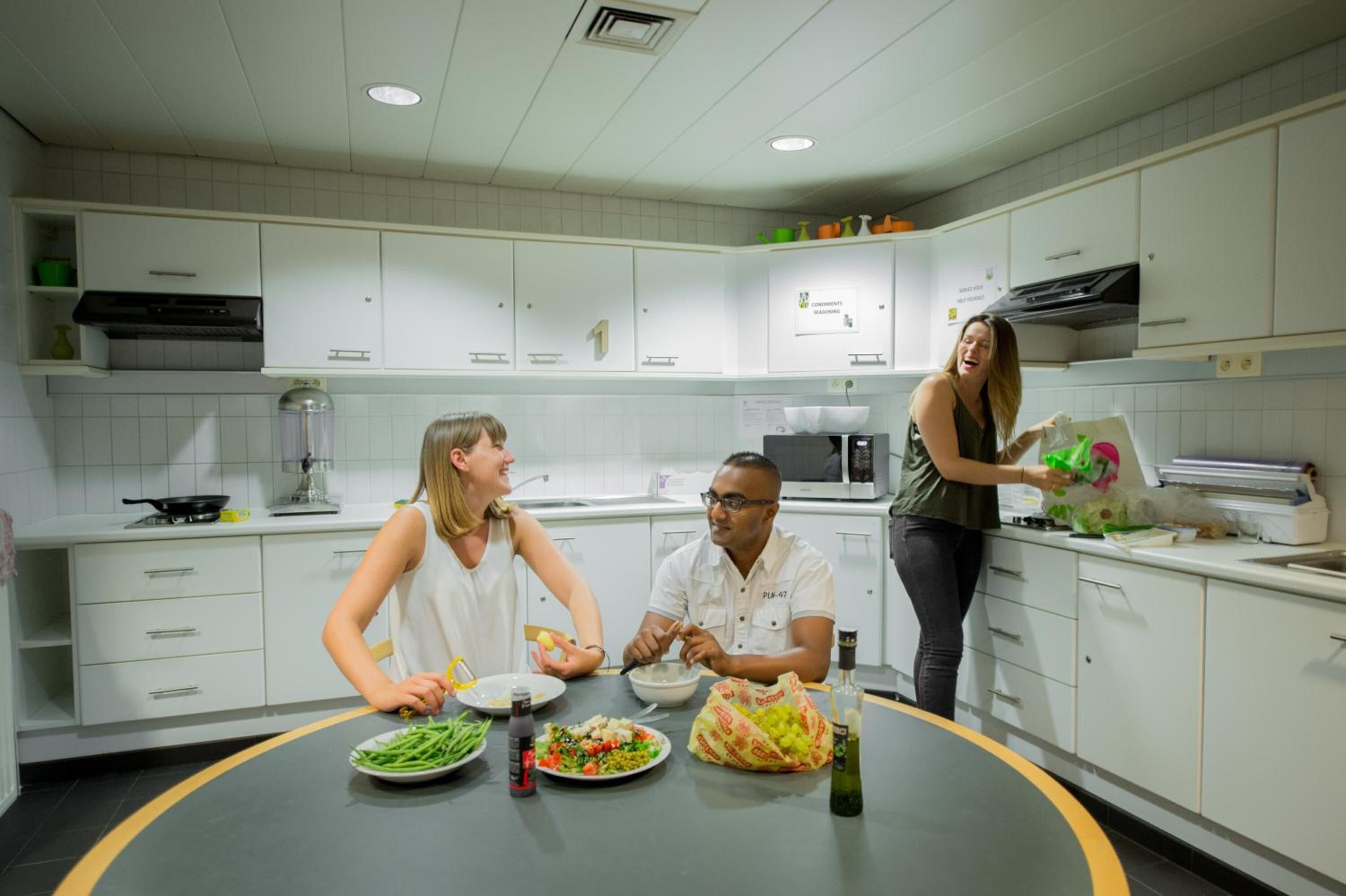 Une cuisine moderne avec des meubles blancs, un plan de travail noir et une table à manger où sont disposés des plats.