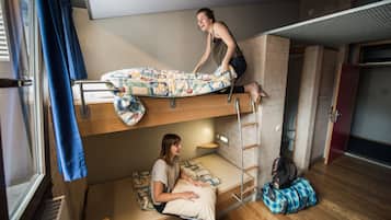 Une chambre avec un lit superposé, une échelle, une fenêtre avec des rideaux et une valise posée sur le sol.
