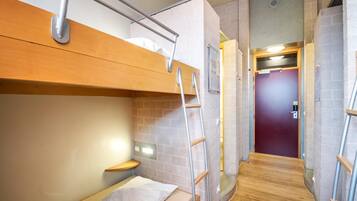 A compact room with a bunk bed, a small wooden table, a ladder, and a door leading to another room.