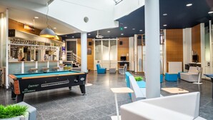 A modern indoor space with a pool table, seating areas, a bar, and a television.