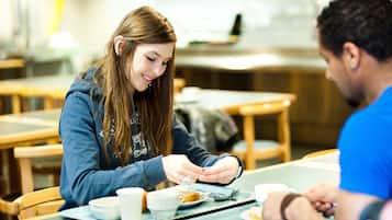 A dining area with tables and chairs, a person using a smartphone, and a tray with food and cups.