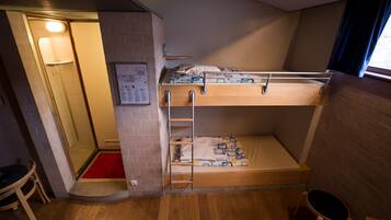 Habitación con literas, piso de madera, un tapete rojo en la entrada, un taburete pequeño y una ventana con cortinas.