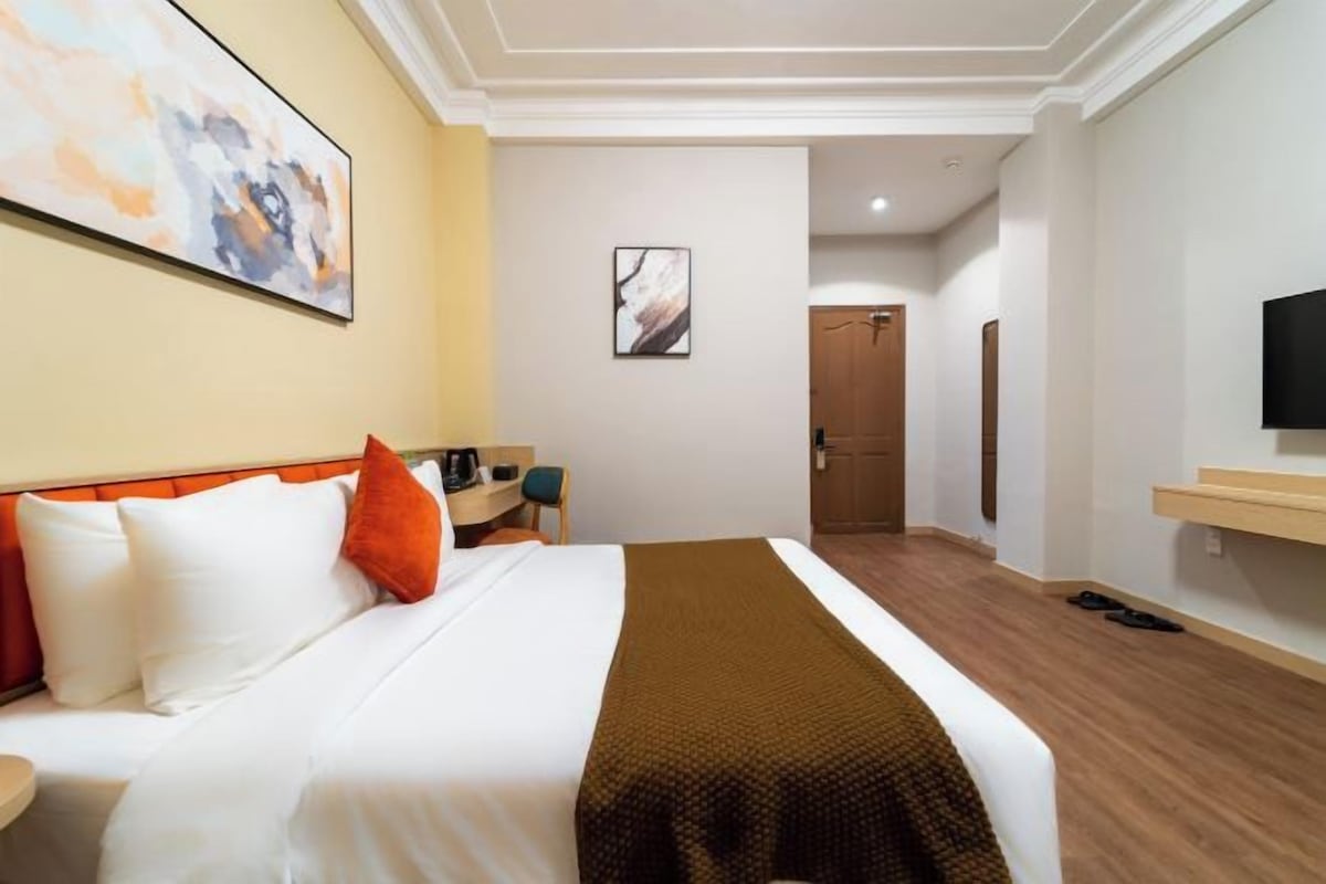 A hotel room with a bed, a desk, a chair, a television, and a door.