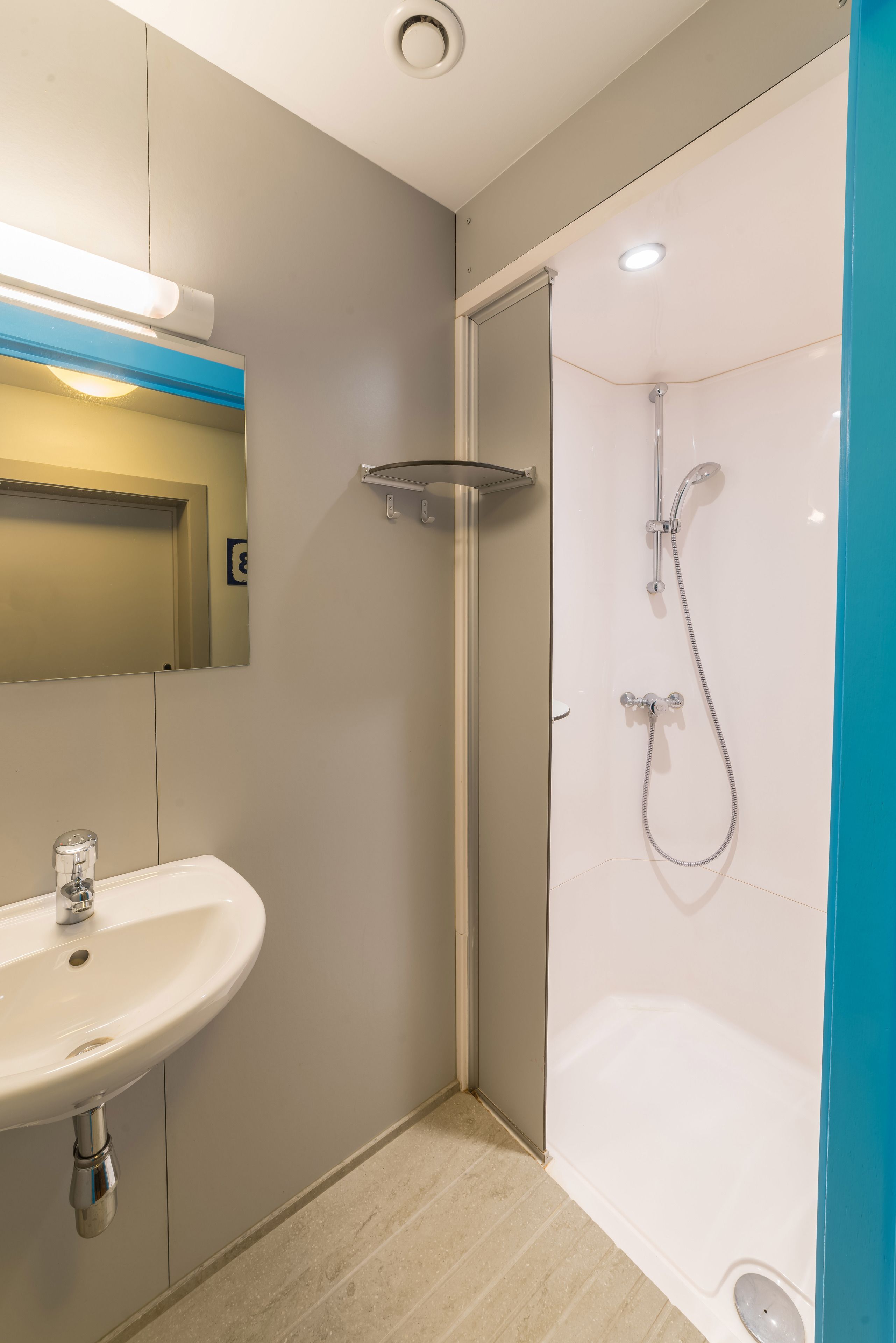 A modern bathroom with a sink, mirror, shower, and a blue accent wall.