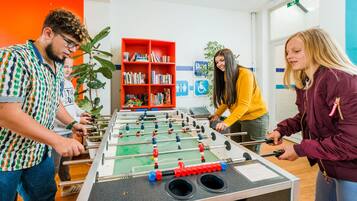 Een tafelvoetbaltafel in een helder verlichte ruimte, met een boekenplank en een plantje op de achtergrond.