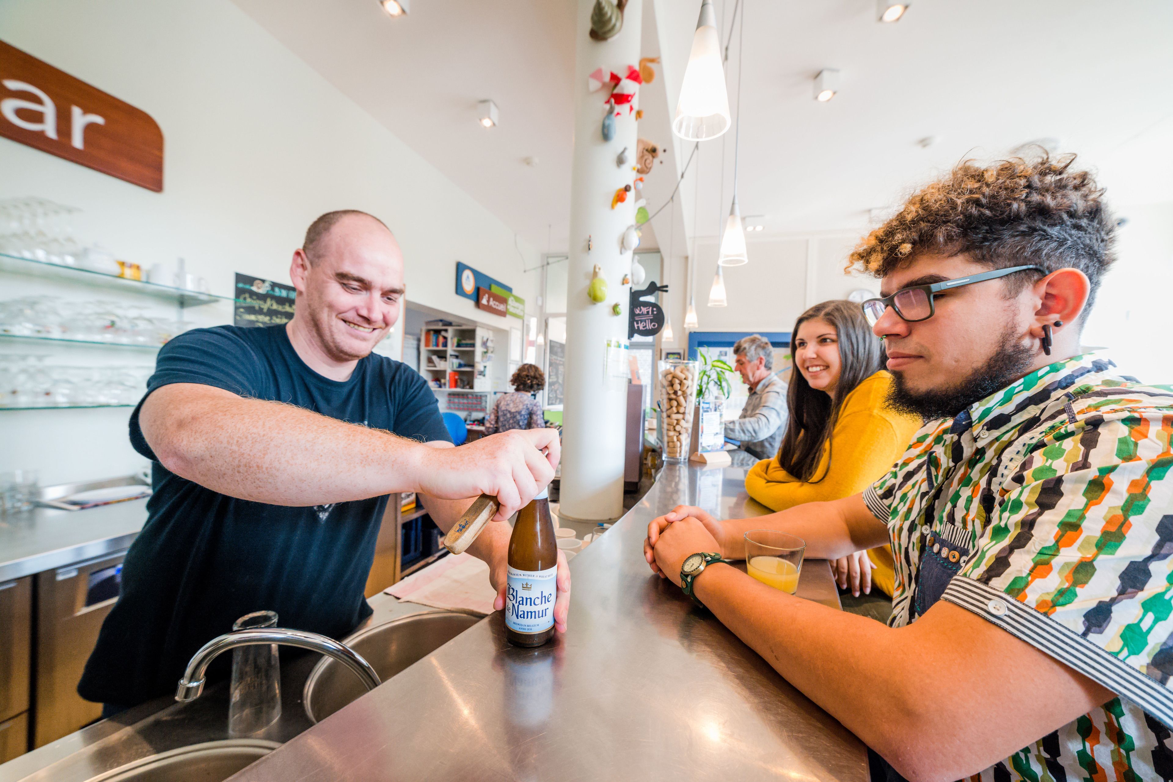 A bar setting with a person pouring a drink, a counter, and shelves with bottles in the background.