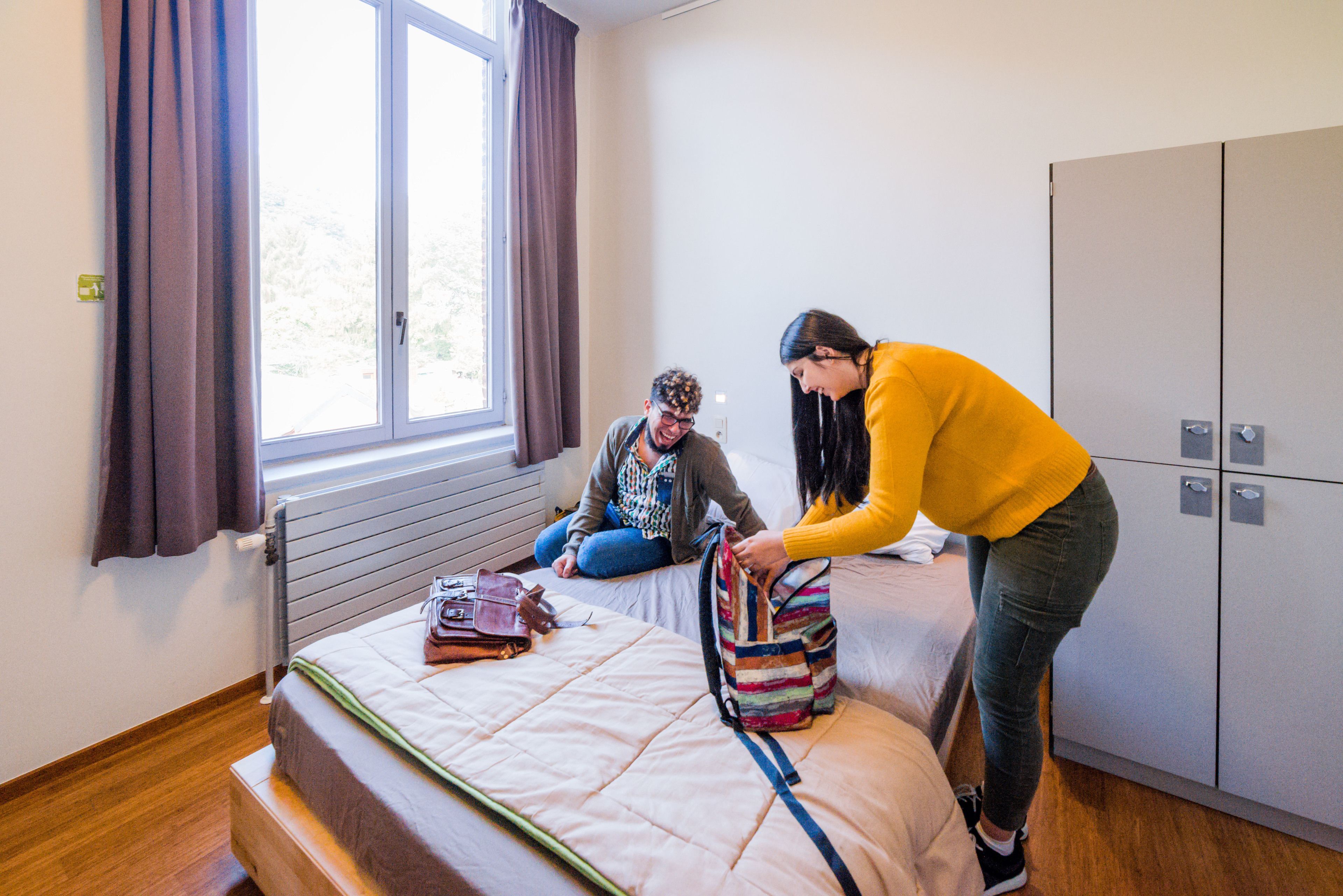 Una habitación con cama, ventana con cortinas, radiador y armario.