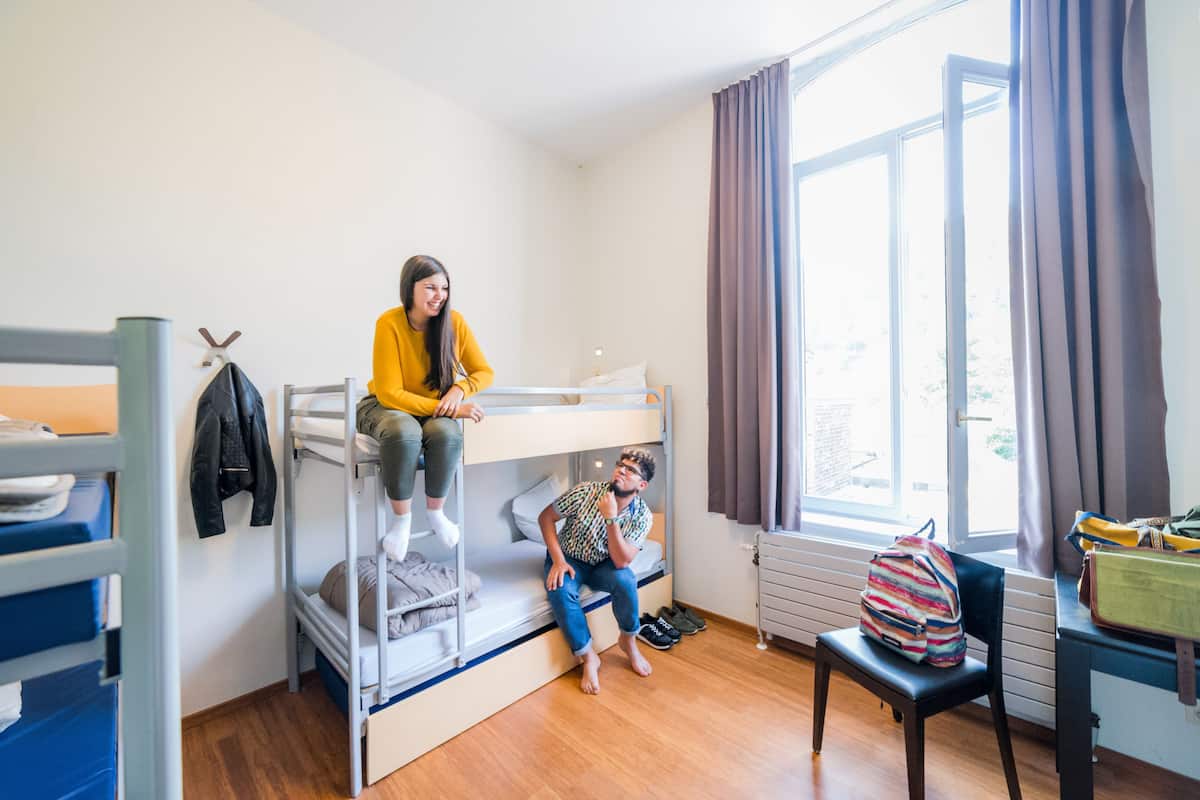 Une chambre de dortoir avec des lits superposés, une fenêtre avec des rideaux, un radiateur et une chaise.