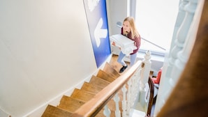 A person descending a wooden staircase with white balusters, carrying a stack of white items. - Auberge de Jeunesse de Namur - Hostel (Namur)