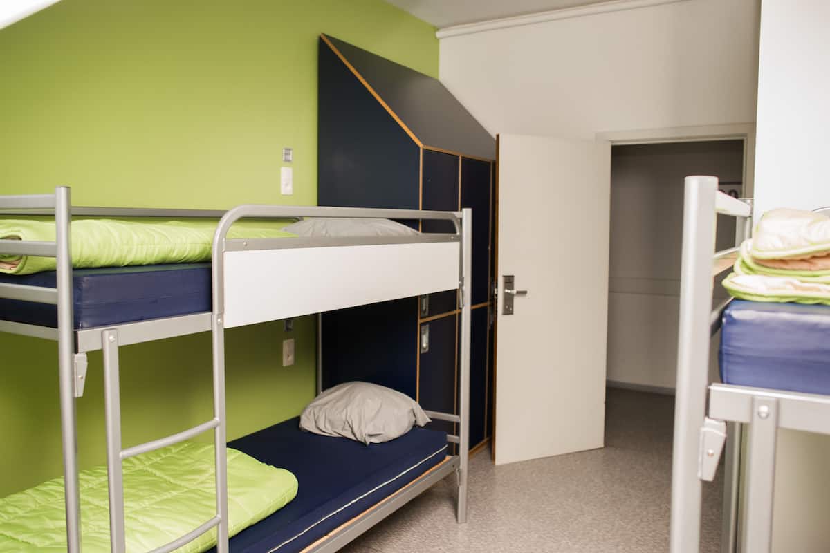 Un dormitorio con literas, una puerta que da a otra habitación y un ventanal pequeño.