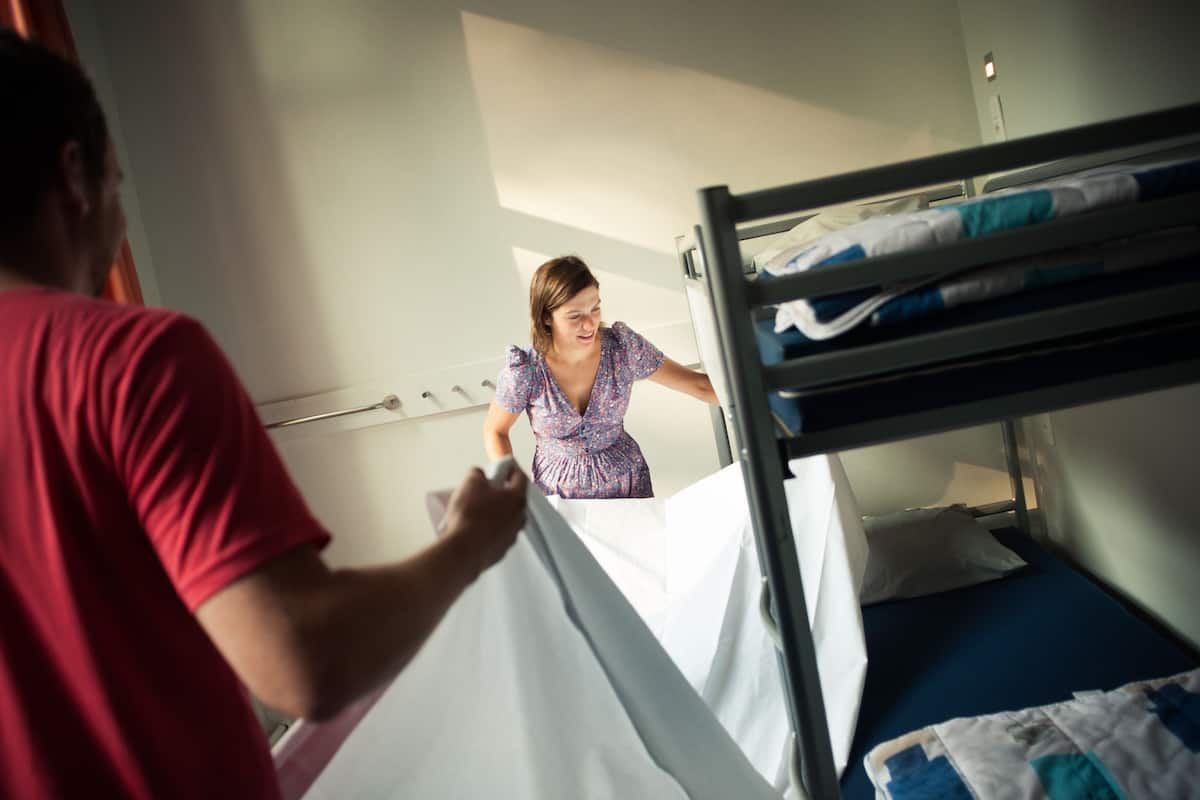 Una cama litera con una persona acomodando la ropa de cama.