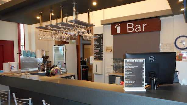 Una zona de bar con un monitor de ordenador, un tablero de menú y un refrigerador.