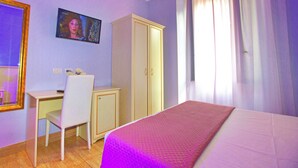 Quarto com cama, escrivaninha, cadeira, guarda-roupa e televisão na parede.