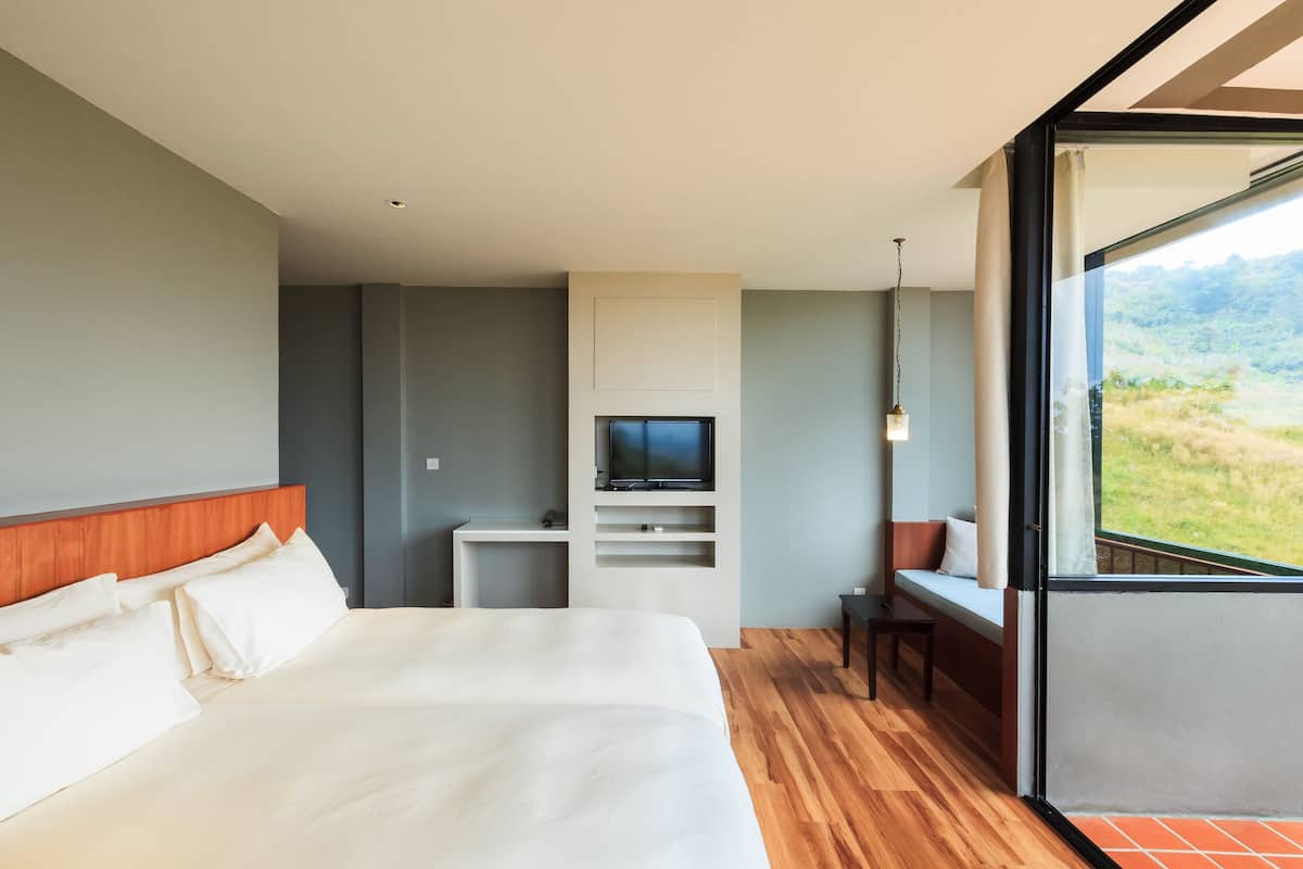 A modern hotel room with a large bed, a TV, a small desk, and a balcony with a view of the outdoors.