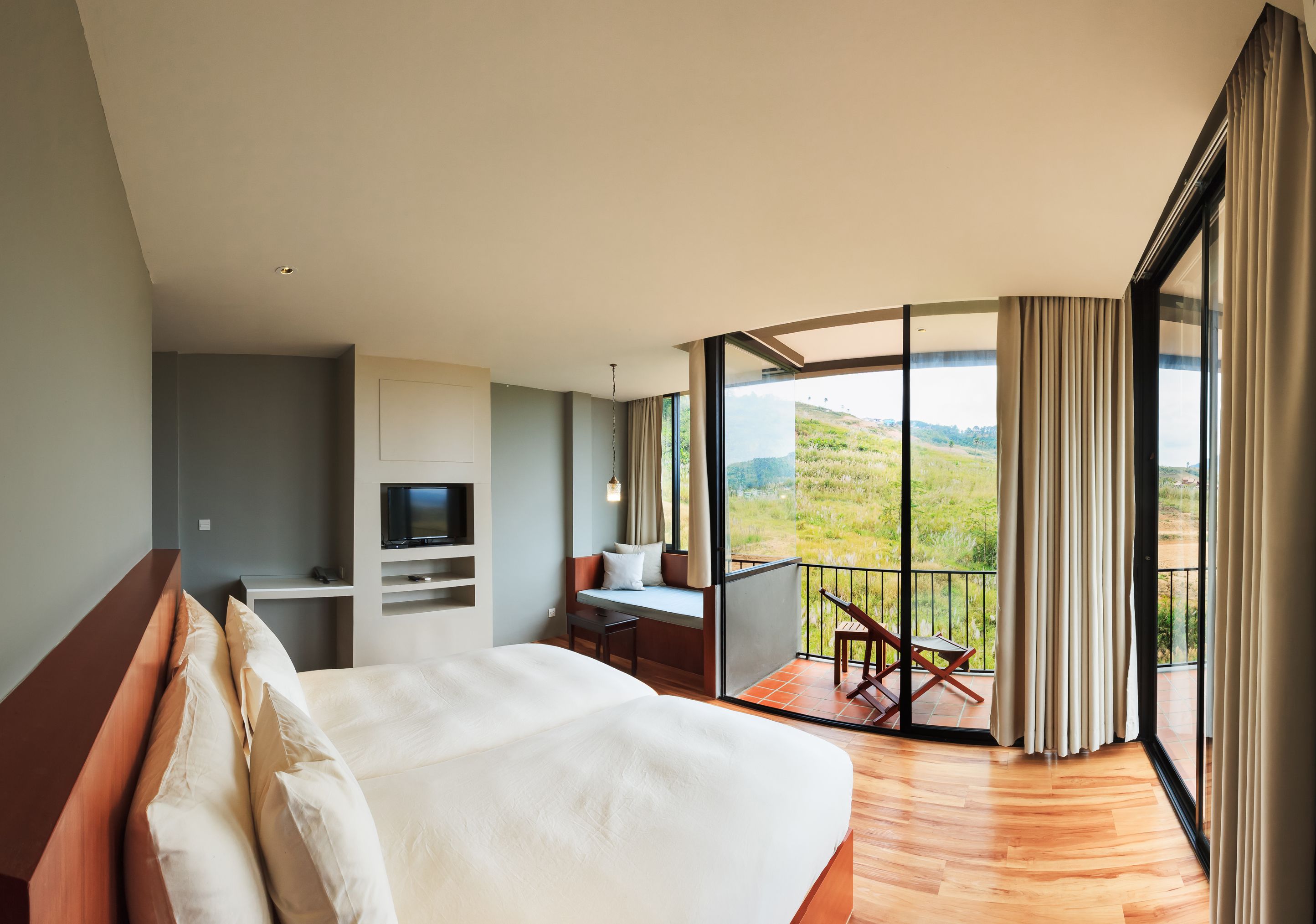 Ein Schlafzimmer mit einem großen Bett, einem Schreibtisch und einem Fernseher. Es bietet einen Balkon mit Blick auf die Landschaft.