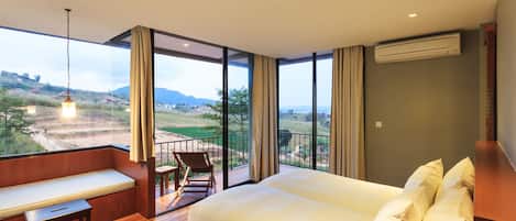 A bedroom with a large bed, a bench, a chair, and a view of a landscape through large windows.