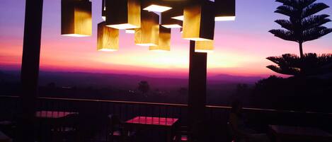 Un restaurante con vista al atardecer, con mesas y sillas de madera, y lámparas colgantes.
