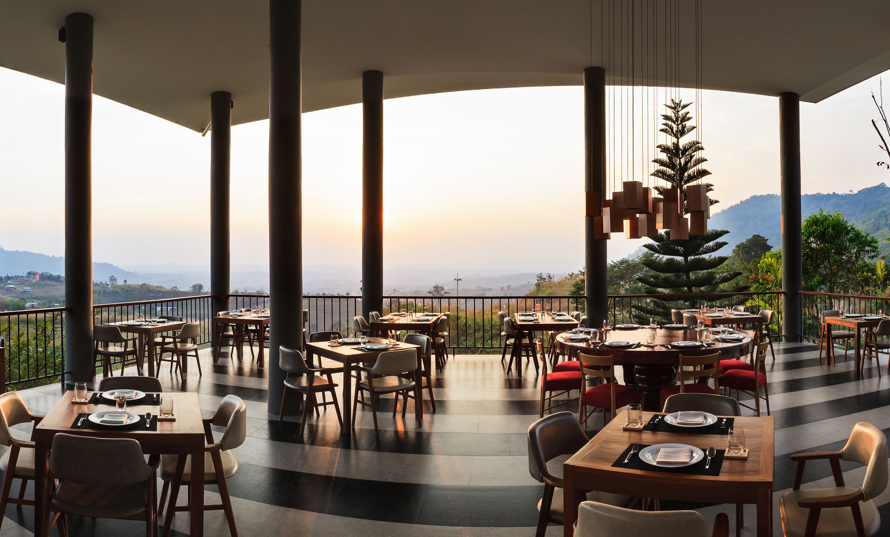 A restaurant with multiple tables and chairs, large pillars, and a view of mountains.