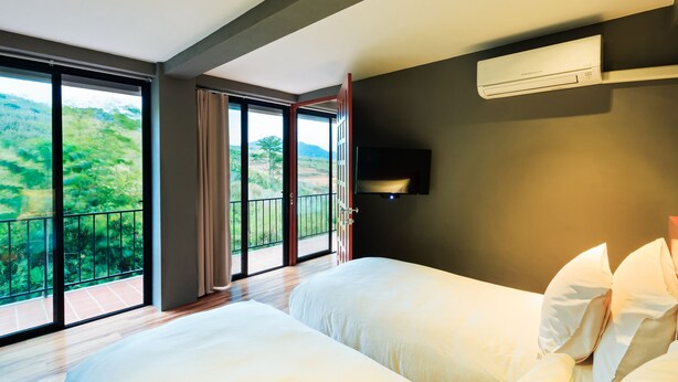 A hotel room with two beds, a large window with a view of greenery, and an air conditioning unit on the wall. - Sirinati Khao Kho National Park (Khao Kho)