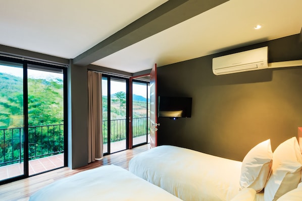 Quarto de hotel com duas camas, uma janela grande com vista para o verde e um ar condicionado na parede.