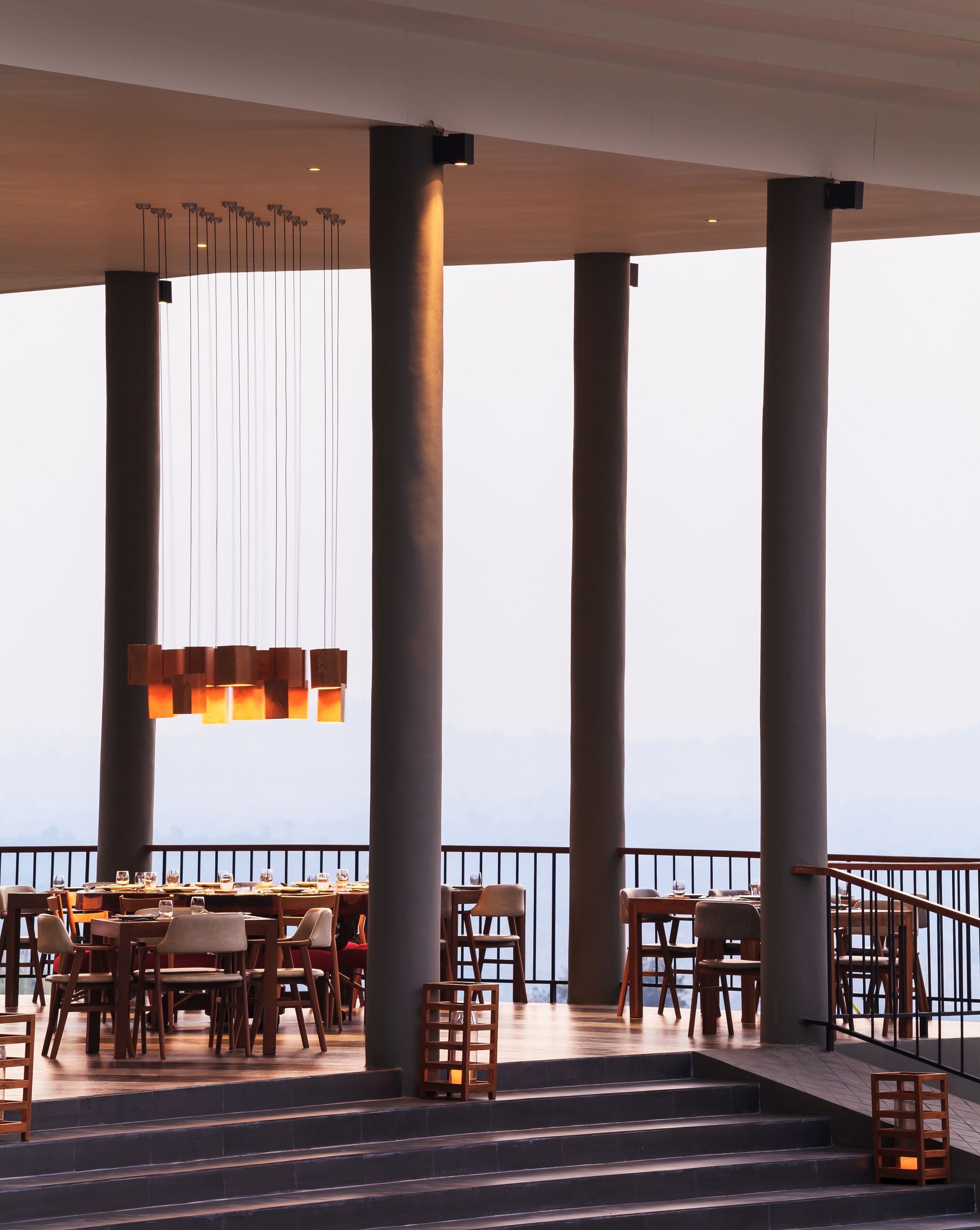 Un restaurant doté d’une terrasse donnant sur un plan d’eau, agrémenté de grandes colonnes et de luminaires suspendus.