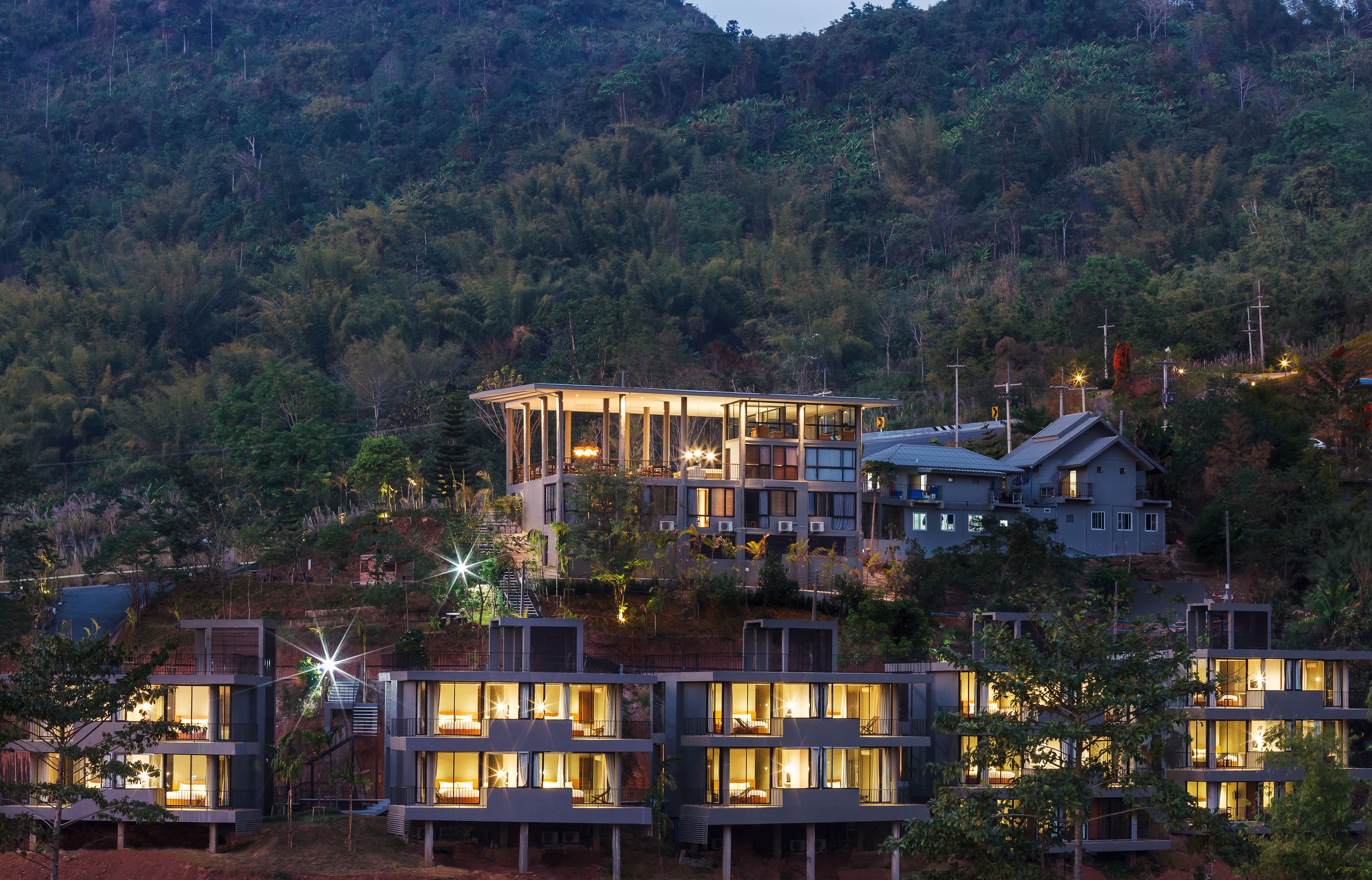 A modern resort with multiple buildings, each featuring balconies and large windows, set against a backdrop of a forested hillside.