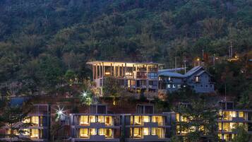 Un resort moderno con varias construcciones, cada una con balcones y ventanas amplias, frente a una ladera boscosa.