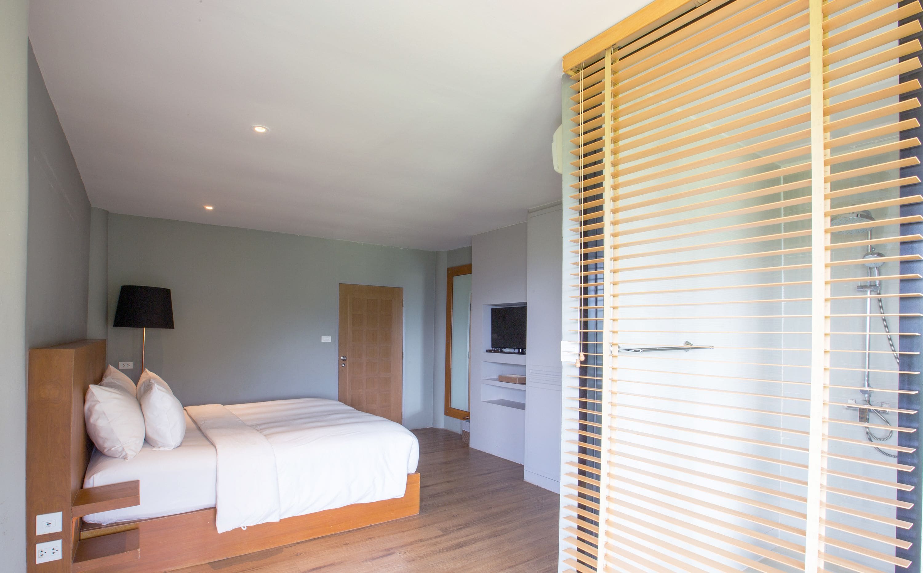 Une chambre à coucher avec un lit, une télévision, une porte en bois et une fenêtre avec des stores.