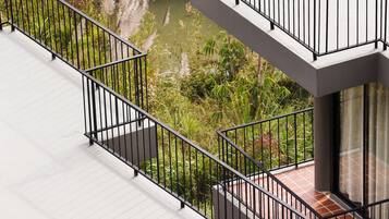 A modern building with a balcony overlooking a body of water, surrounded by greenery.