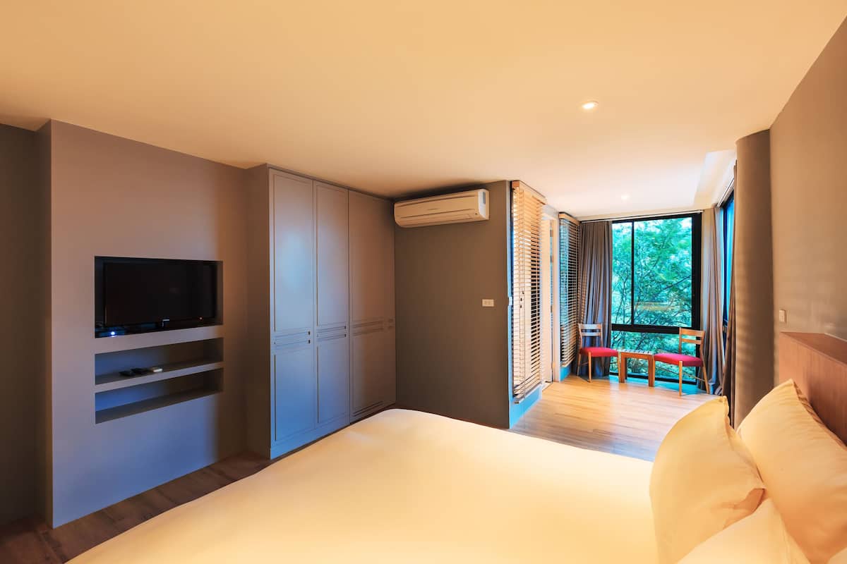A modern bedroom with a large bed, built-in TV, wardrobe, and a view of the outdoors through a window.