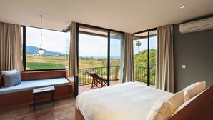 A bedroom with a large bed, a bench, and a view of a green landscape through large windows. - Sirinati Khao Kho National Park (Khao Kho)