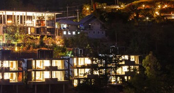 Un edificio moderno con varios balcones y ventanas amplias, rodeado de árboles y otros edificios.
