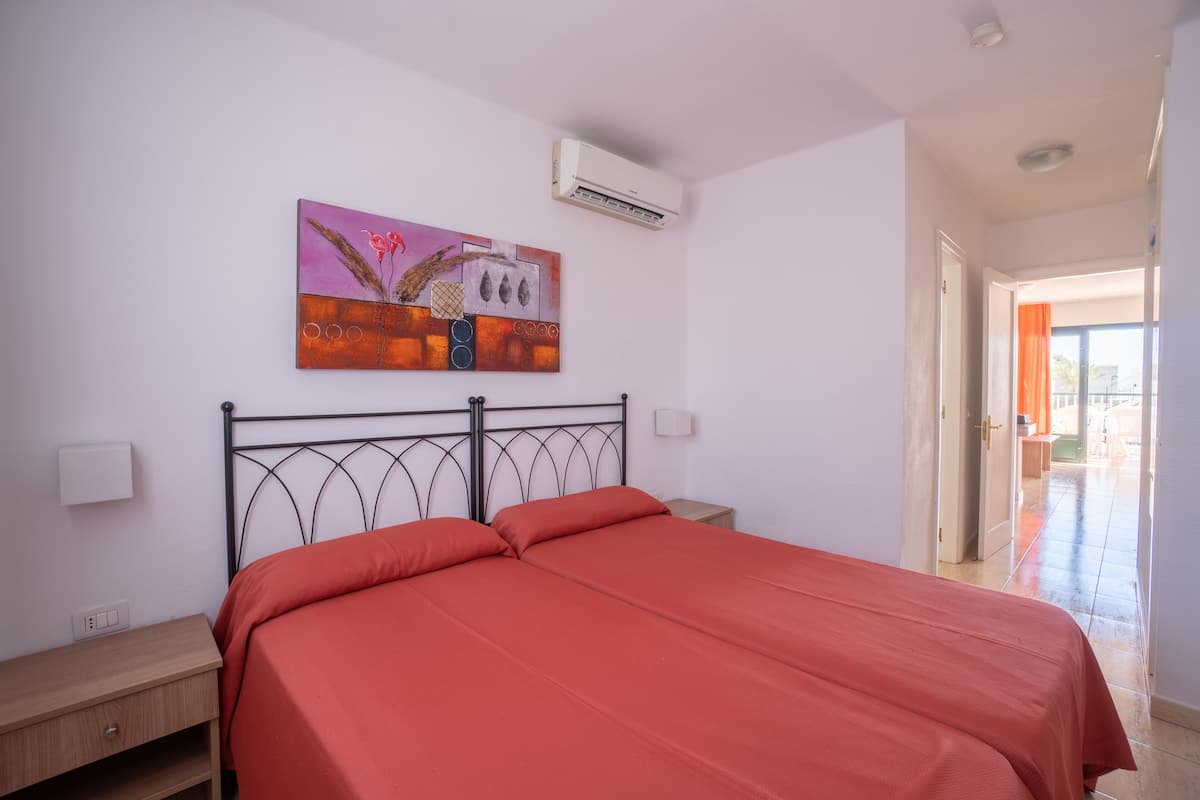 Ein Schlafzimmer mit Bett, Nachttisch, Wandairconditioner und einem Gemälde.