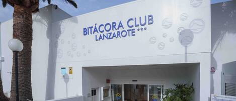 The exterior of the Bitácora Club Lanzarote, featuring a modern facade, palm trees, and a clear sky.