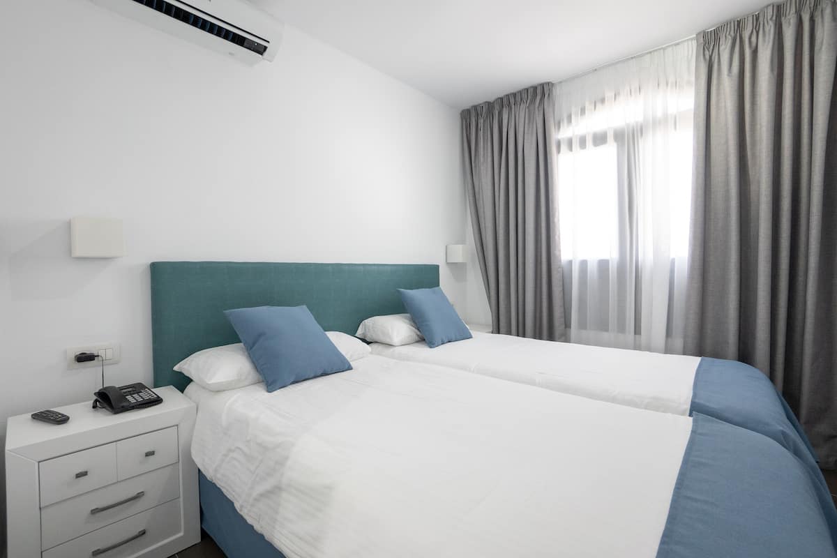 Ein Hotelzimmer mit zwei Betten, einem Nachttisch mit Telefon und einem Fenster mit Vorhängen.
