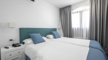 Habitación de hotel con dos camas, una mesita de noche con teléfono y una ventana con cortinas.