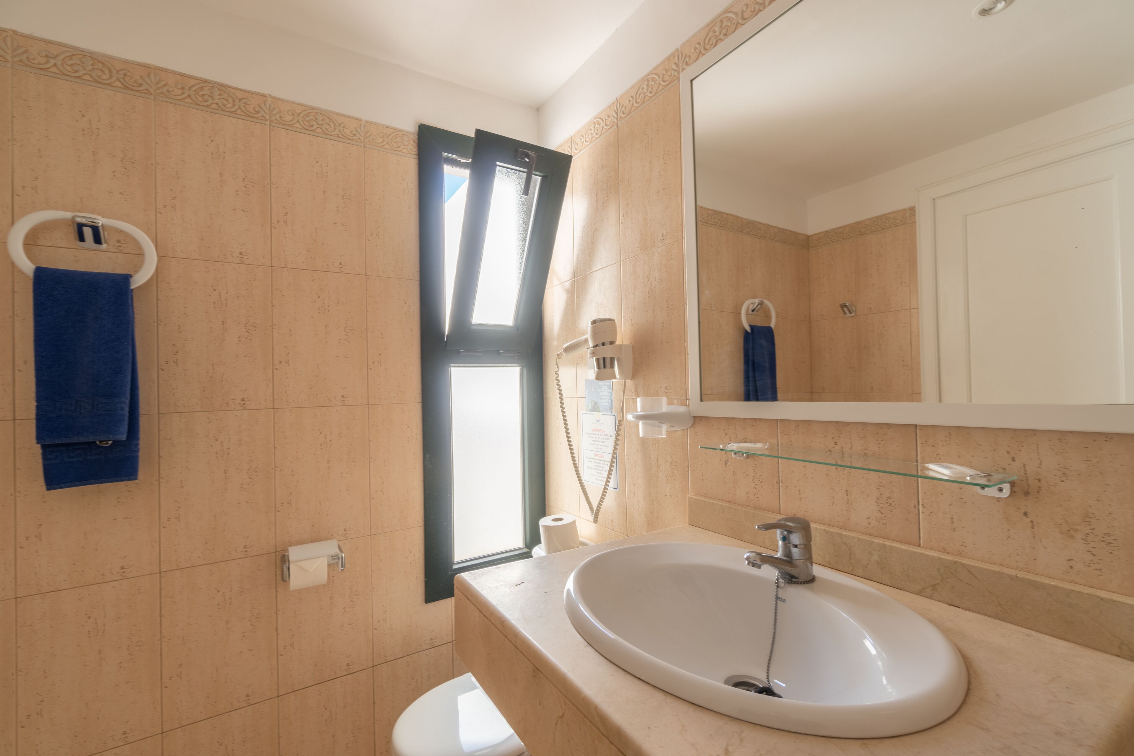 Un baño con lavamanos blanco, espejo, toallero y retrete.